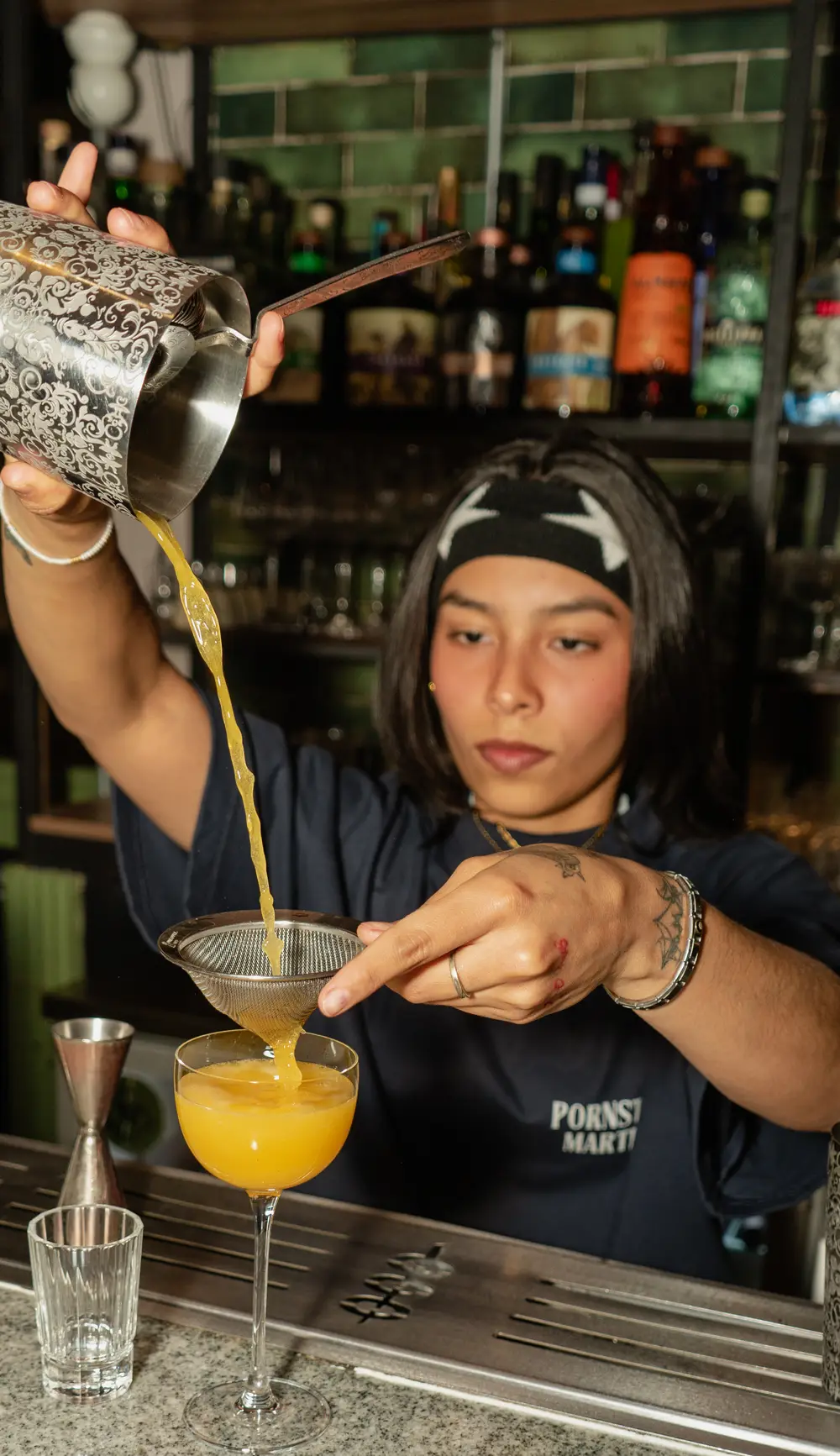 Bartender preparando un cocktail detrás de la barra con una playera The Last Drop